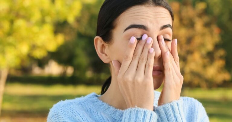Persona con molestias en los ojos en un entorno otoñal, ilustrando las alergias estacionales.